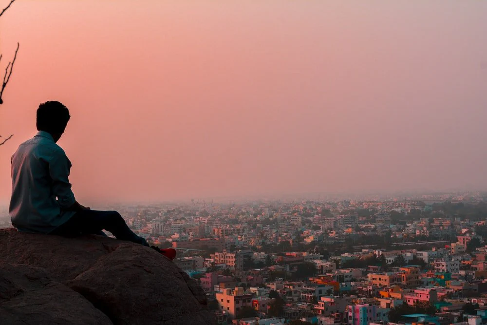 Paint By Numbers | Hyderābād - Man Sitting On Rock Formation Facing On Buildings During Daytime