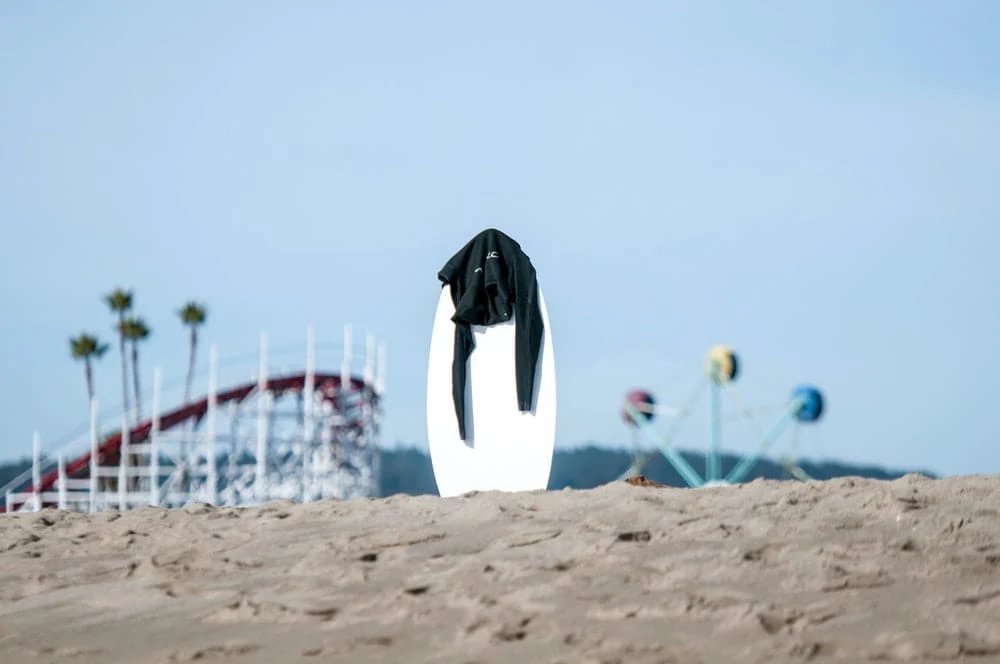 Paint By Numbers | Santa Cruz - White Surfboard With Black Rashguard On Top In The Middle Of Sand