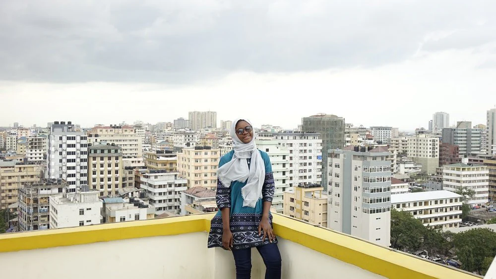 Paint By Numbers | Dar Es Salaam - Woman In White Long Sleeve Shirt And Blue Denim Jeans Standing On Yellow Concrete Wall During